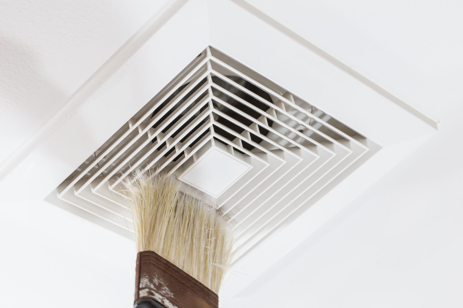 A paint brush cleaning a white bathroom ceiling vent.