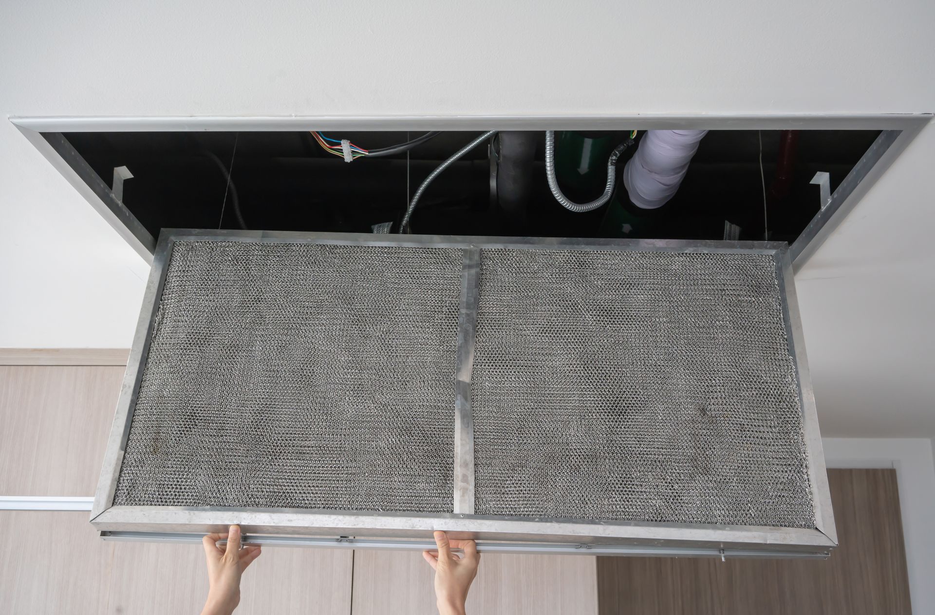 Hands holding a large air filter panel removed from a ceiling vent.