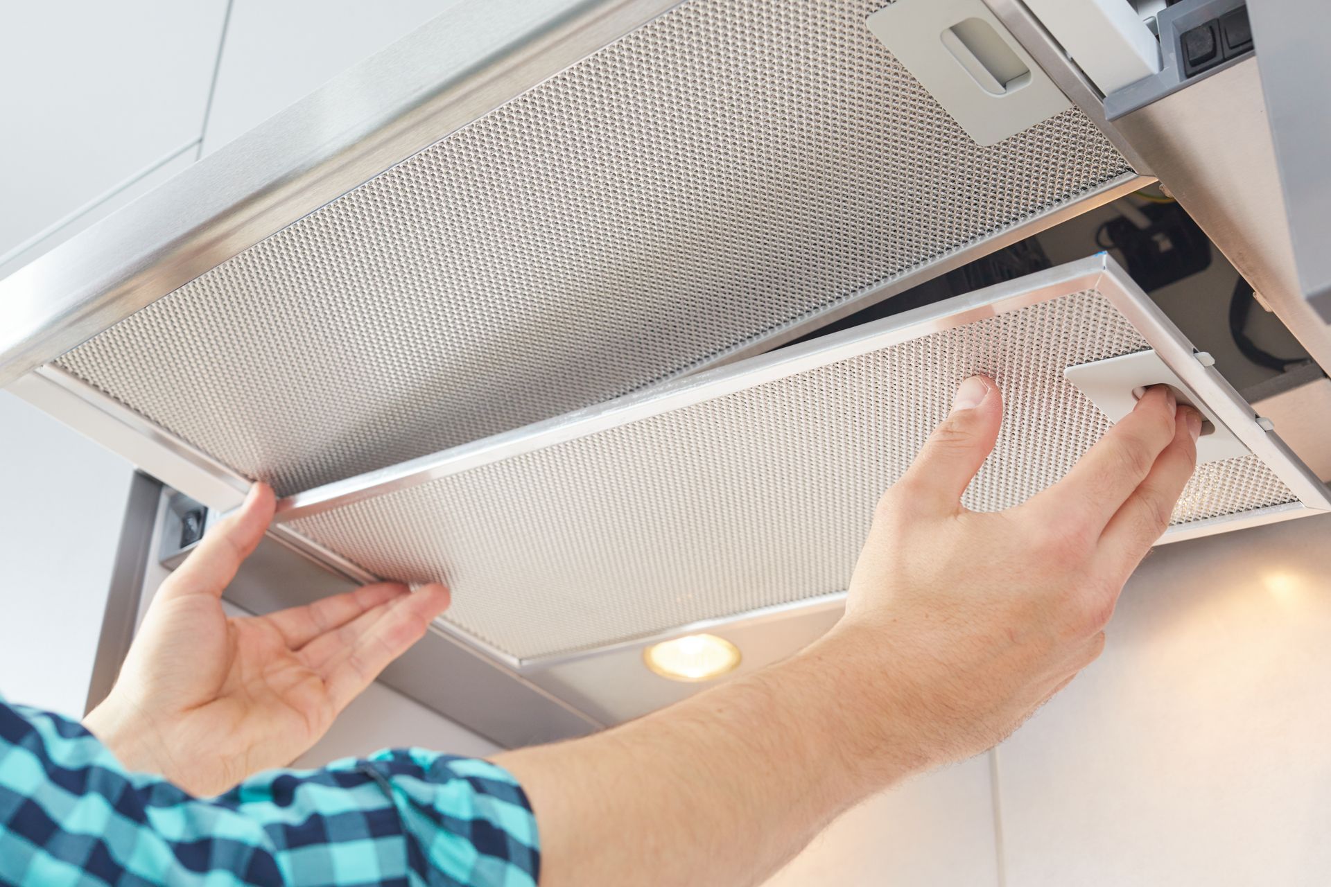 Hands removing a metal range hood filter from its housing.