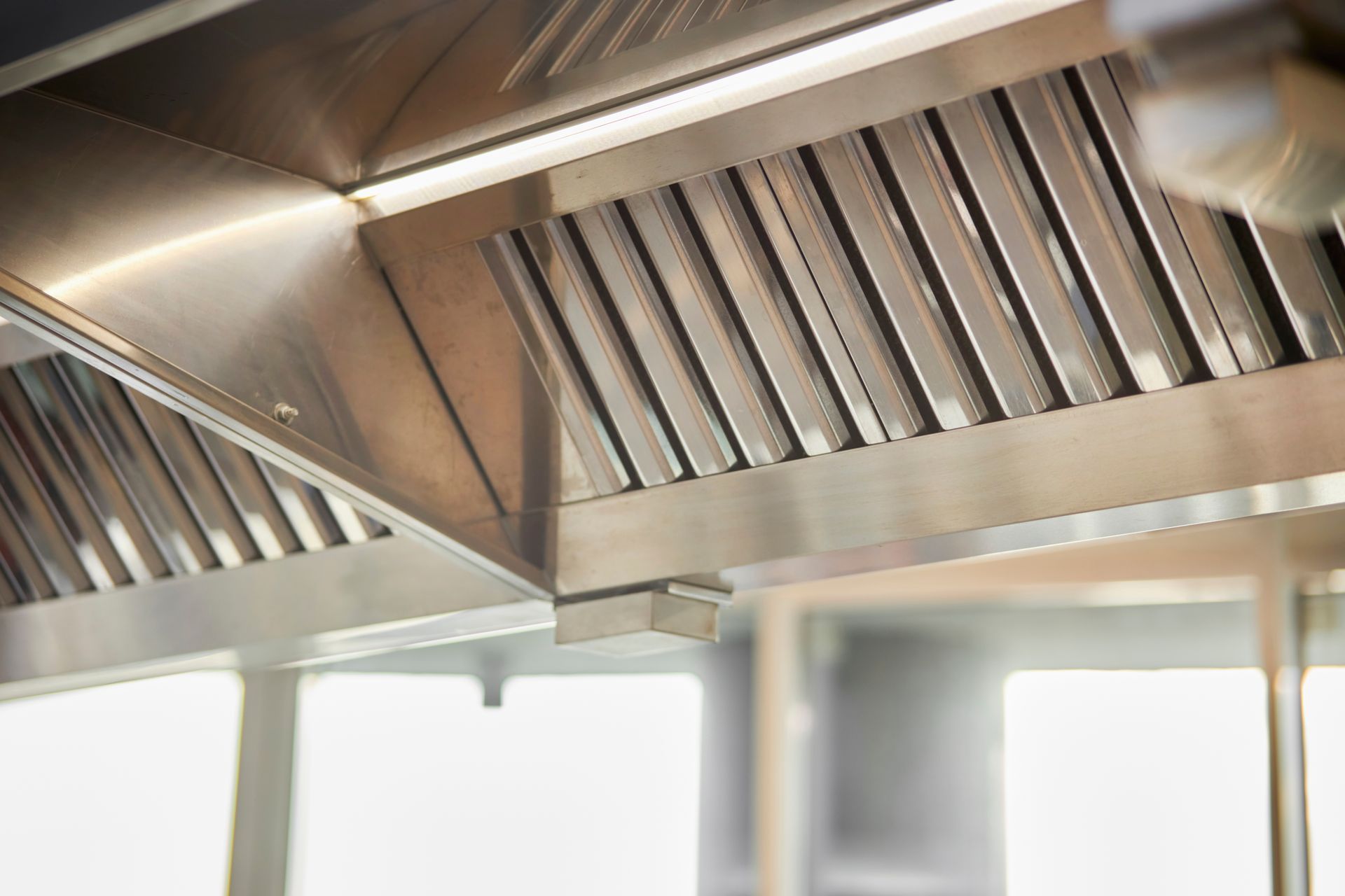 Close-up of a commercial kitchen exhaust hood with angled stainless steel baffles.
