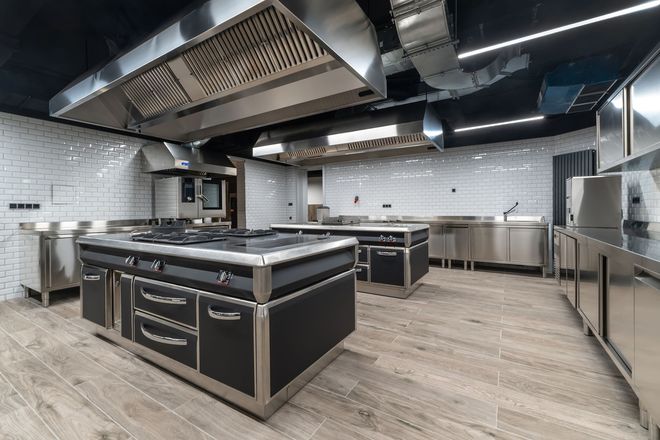 Modern commercial kitchen with stainless steel appliances, black accents, and tile walls.