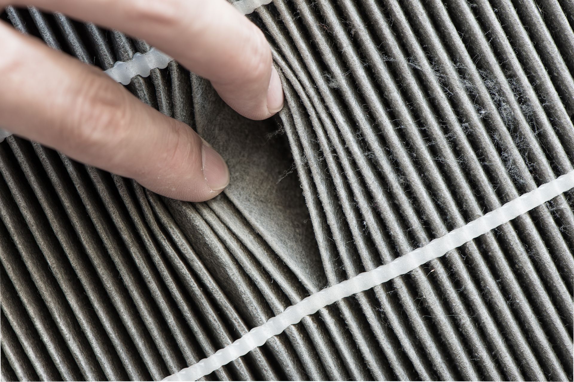 Hand touching a very dirty, gray air filter with visible debris.