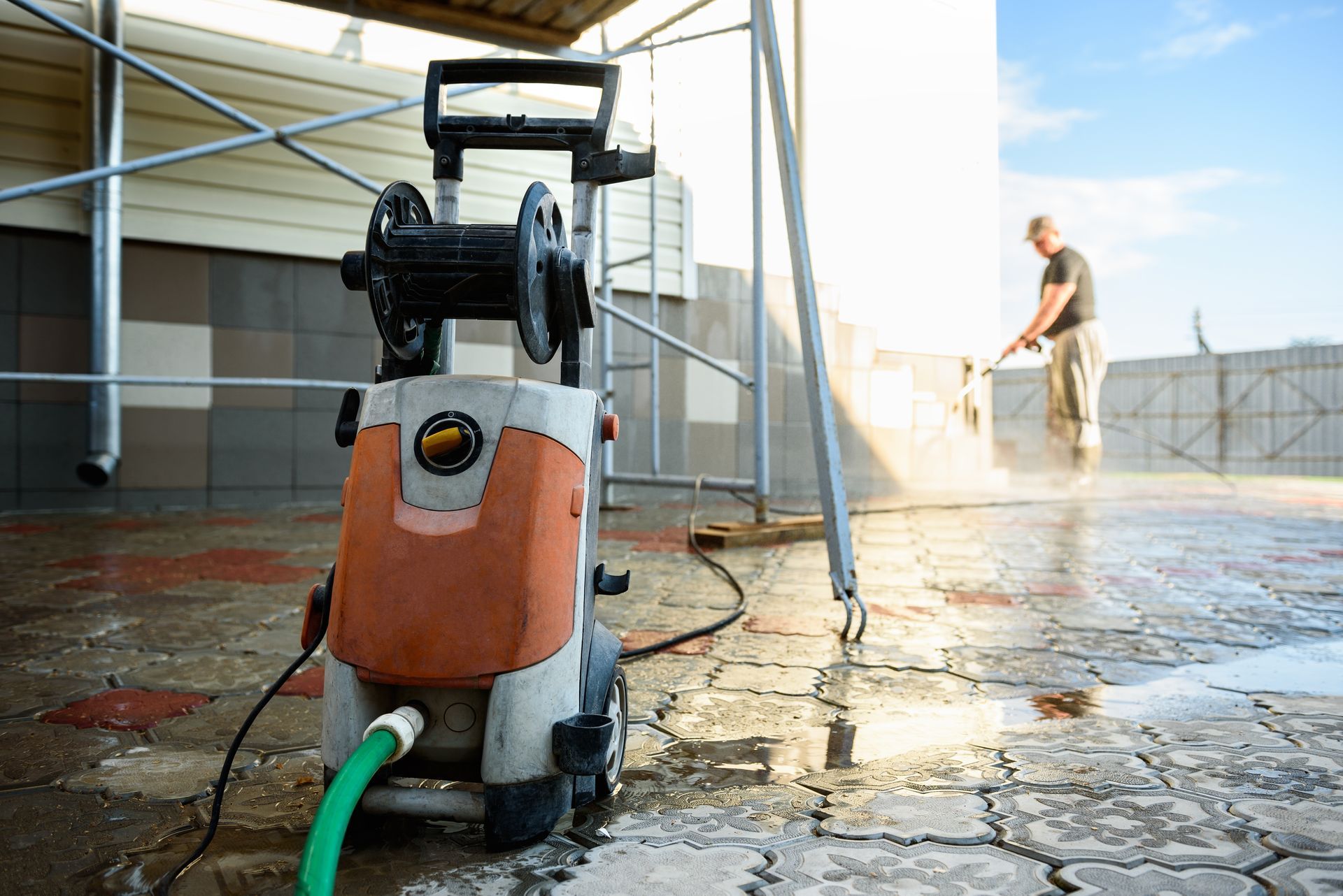 Pressure washer cleaning a tiled patio; person spraying in background.