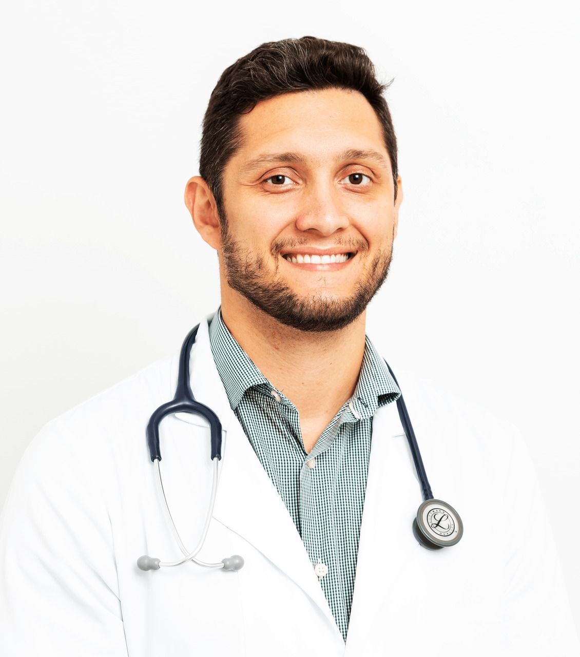 Médico sorridente vestindo um jaleco branco, estetoscópio e uma camisa estampada, em um estúdio.