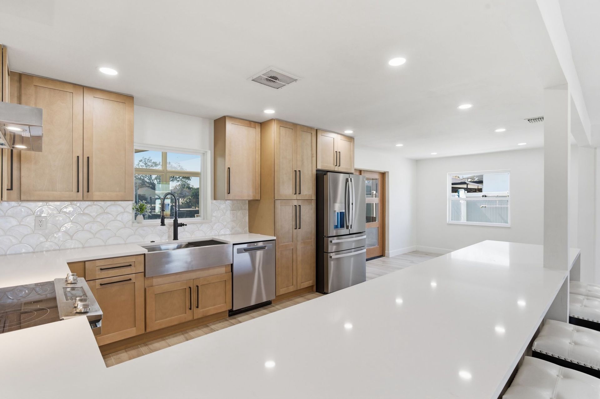 Modern kitchen with light wood cabinets, white quartz countertops, stainless steel appliances, and a farmhouse sink.