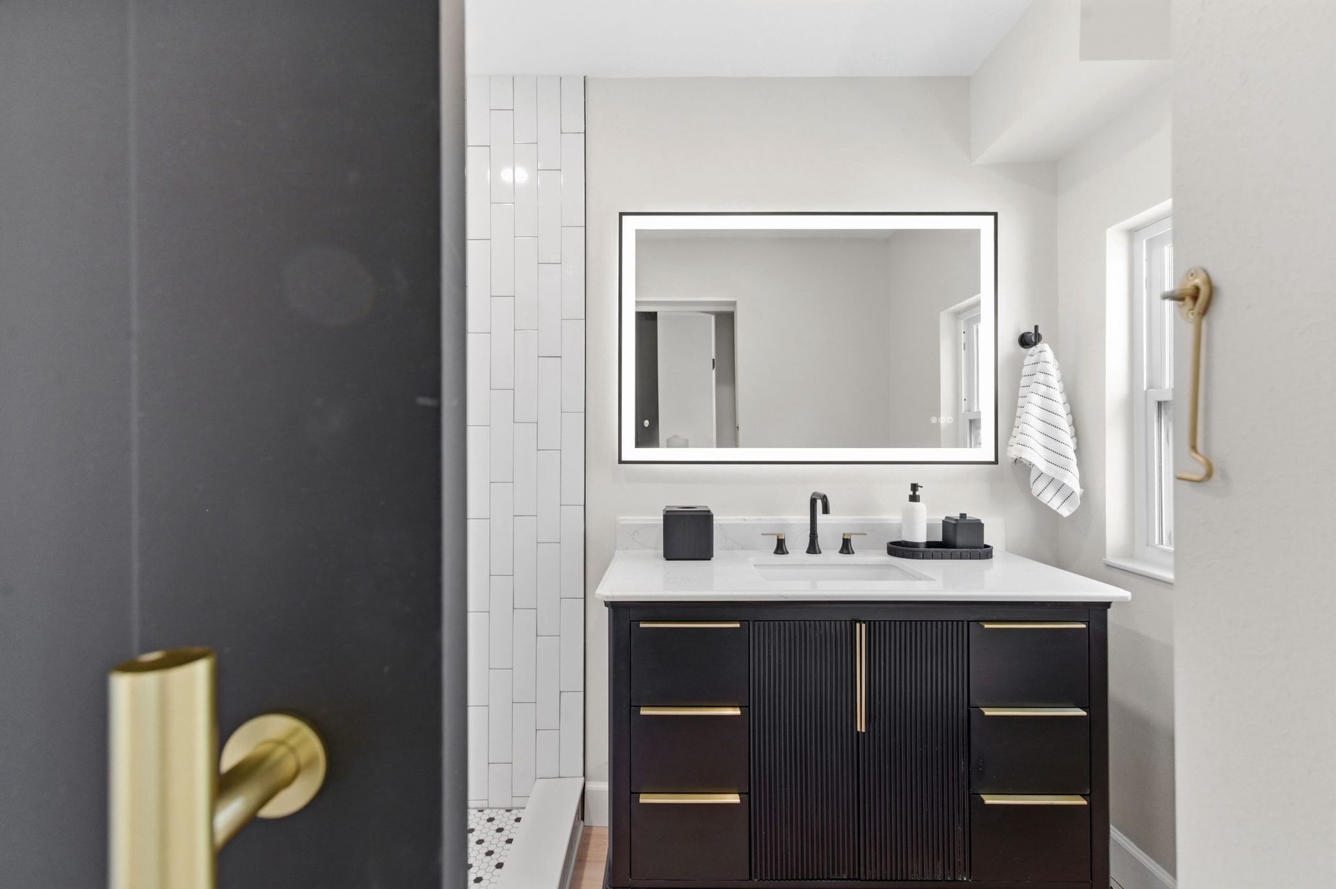Modern bathroom with dark vanity, illuminated mirror, and white tiled shower.