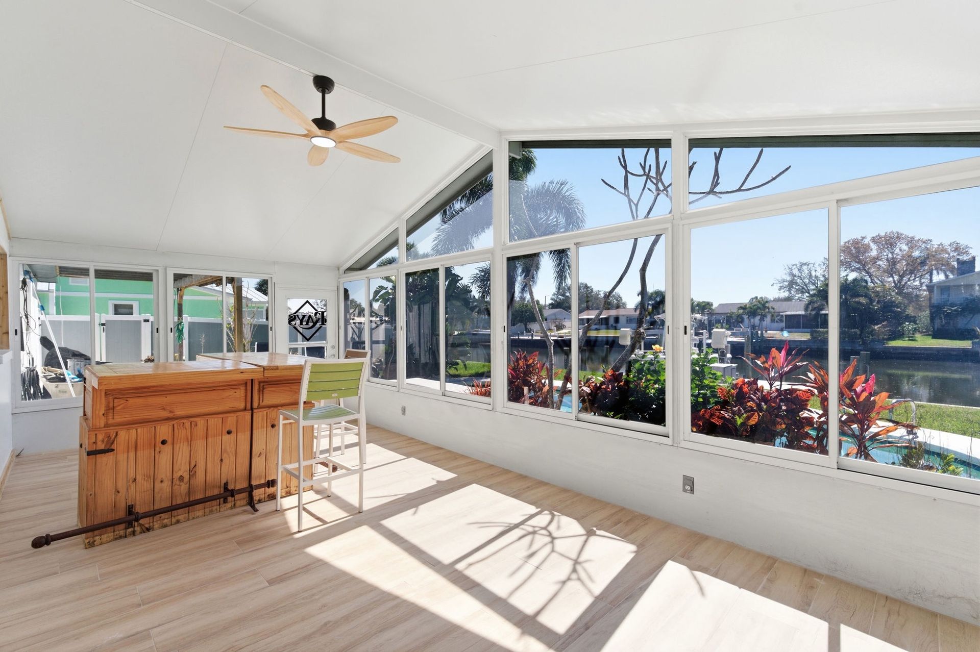 Sunroom featuring a wooden bar, stool, ceiling fan, and large windows with a canal view.