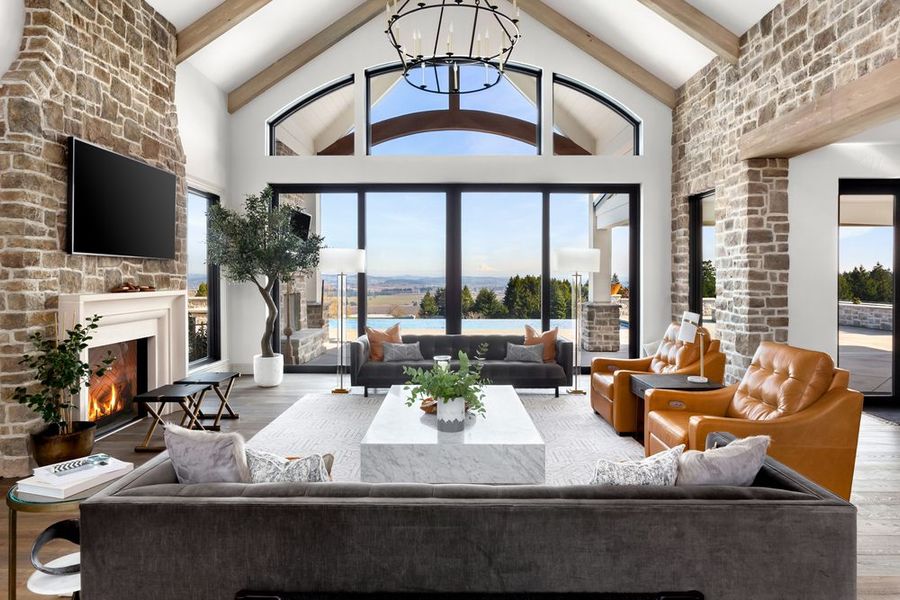 Living room with stone fireplace, large windows, and views of the landscape.
