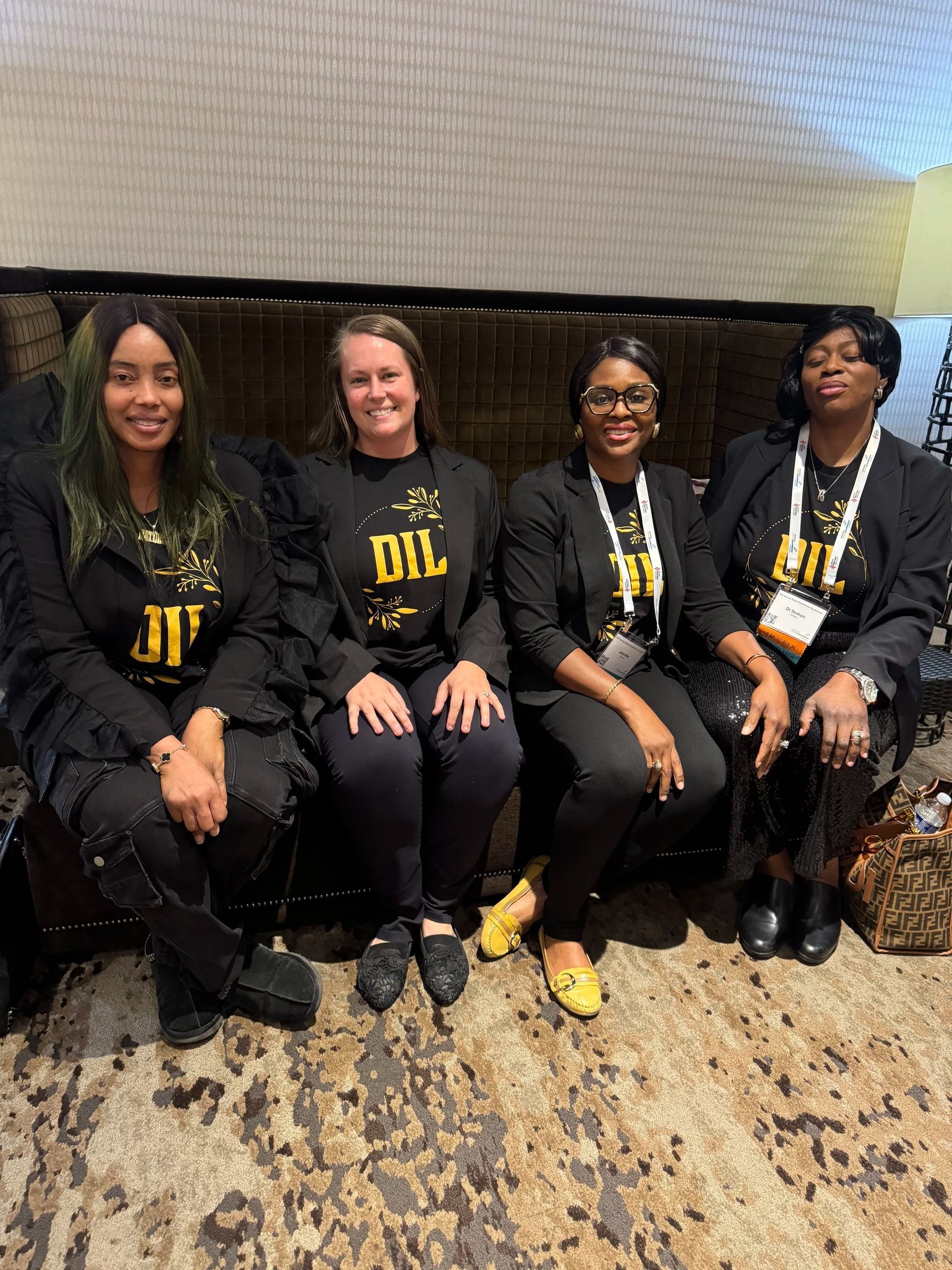 Four people seated on a couch, smiling in black outfits at an indoor event.