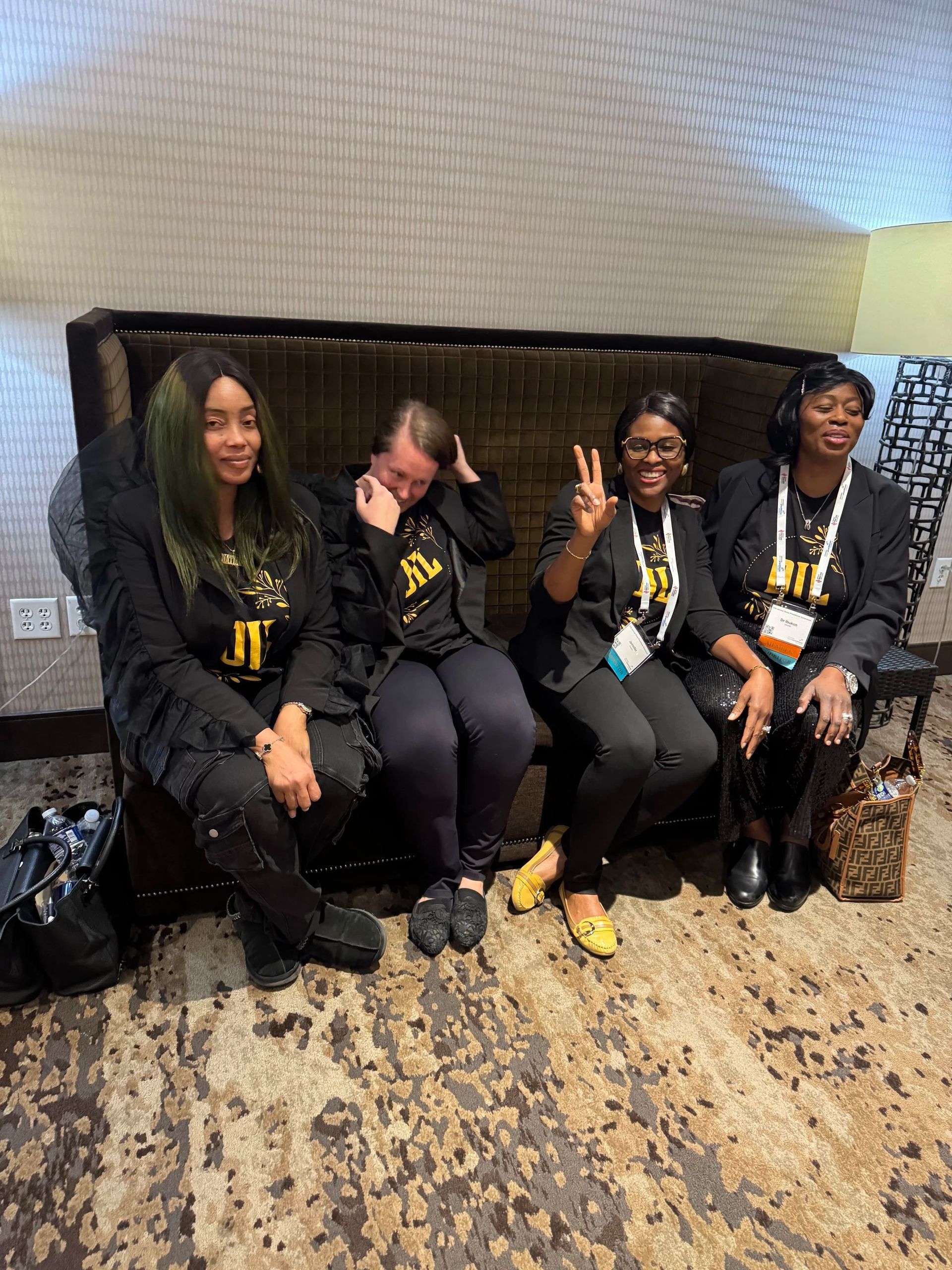Four people in black hoodies sit on a bench indoors, smiling and posing with yellow lanyards.