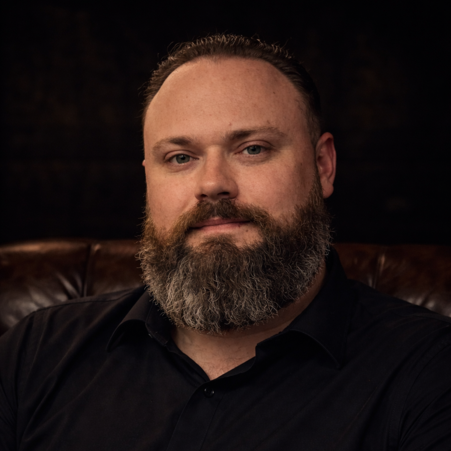Man wearing a black hat and shirt smiles in front of a brick wall.