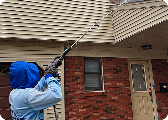 Person using a long-handled pressure washer on a house exterior near a brick wall and door