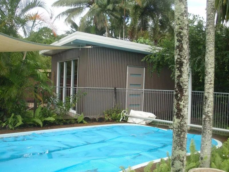 A Small House Next To A Large Swimming Pool Surrounded By Palm Trees — Justmill Carpentry & Building in Smithfield, QLD
