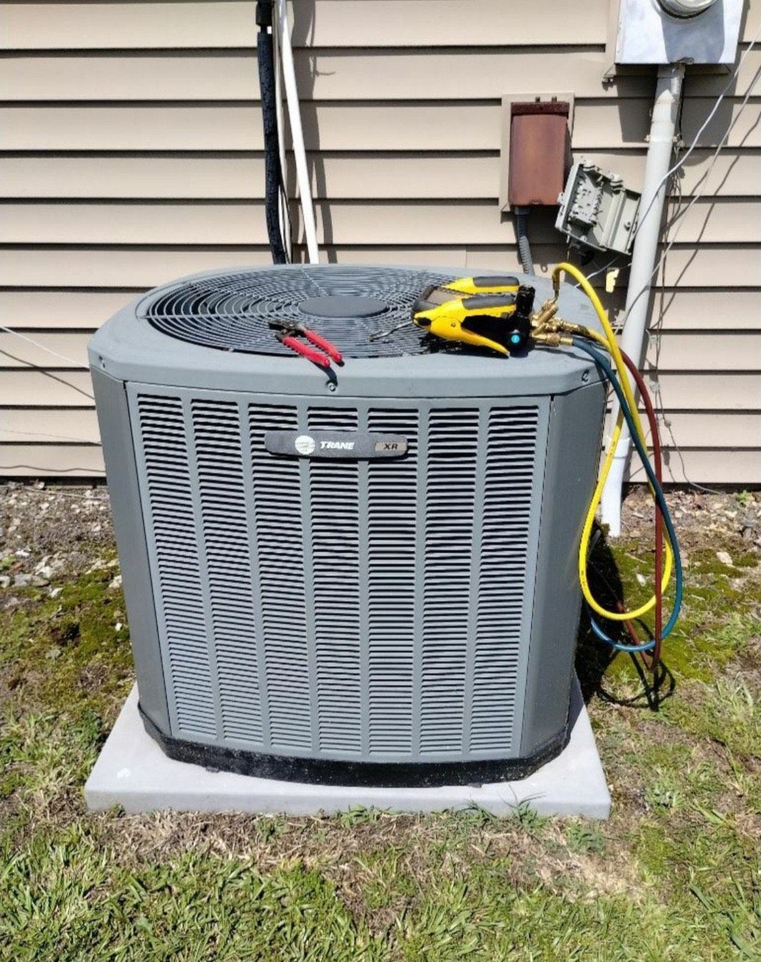 An air conditioner is being serviced outside of a house.