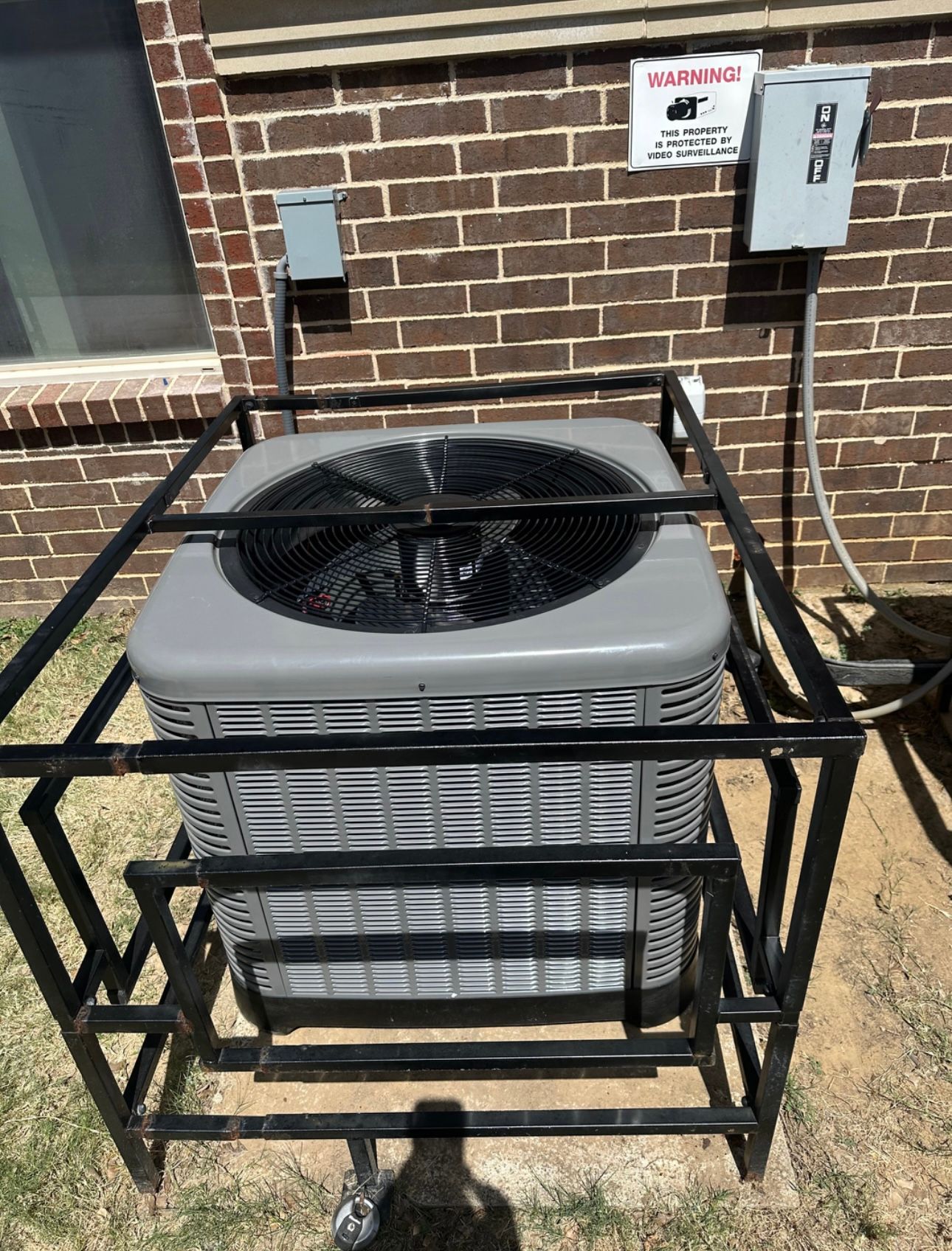 An air conditioner is sitting in a metal cage on the side of a brick building.