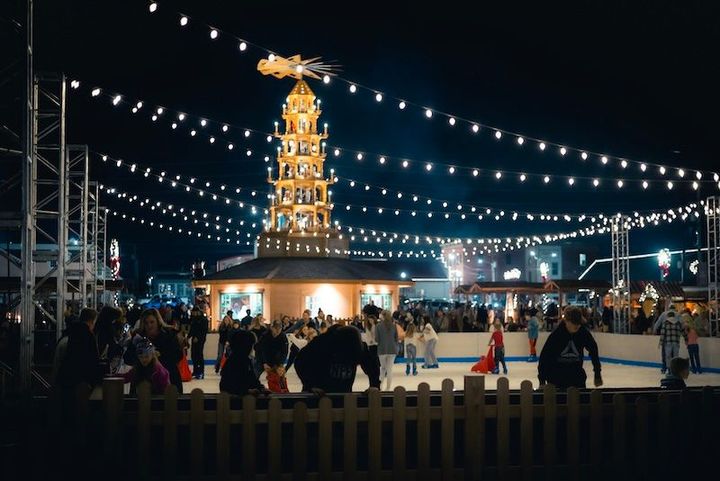 A group of people are ice skating in front of a christmas tree.