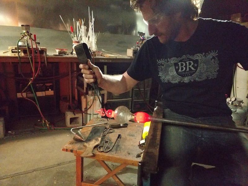 A man wearing a br shirt is blowing glass