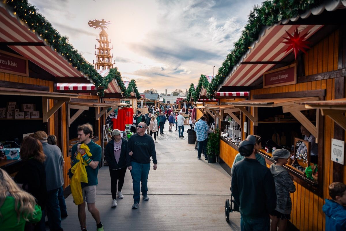 A group of people are walking down a street in front of a christmas market.