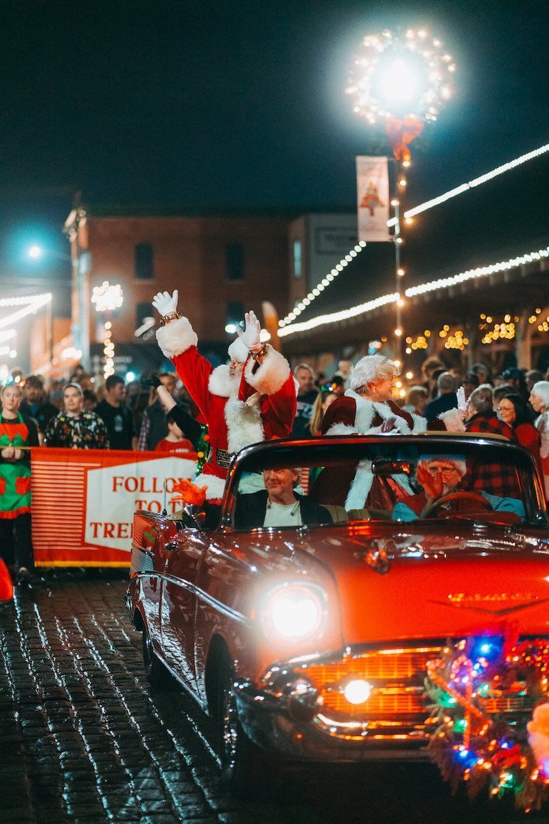 Santa claus is driving a red car in a parade.
