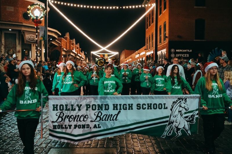Holly pond high school brence band is marching down the street in a parade.