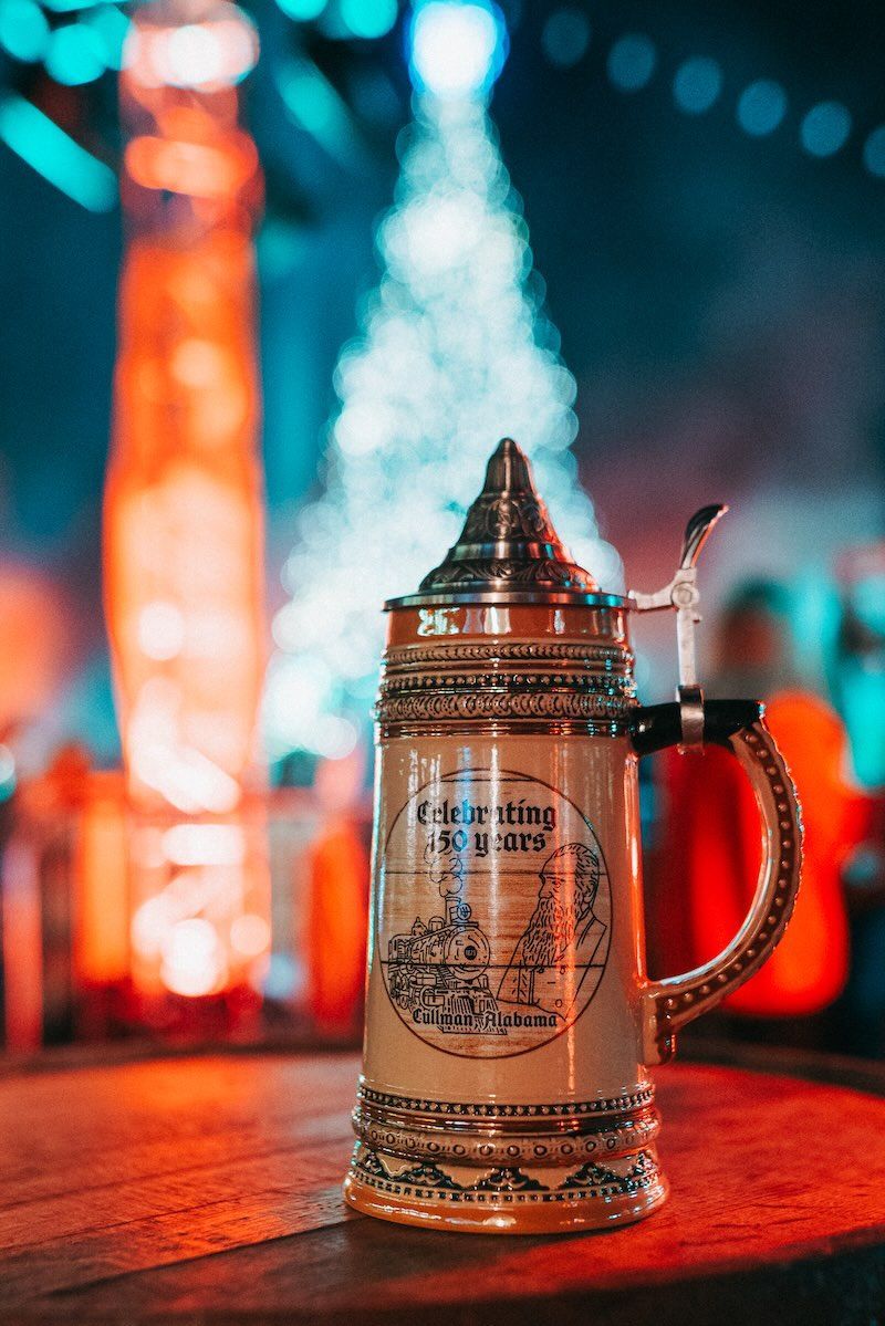 A beer mug is sitting on a wooden table in front of a christmas tree.
