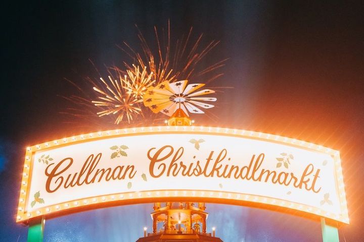 A sign that says cullman christkindlmarkt with fireworks behind it.