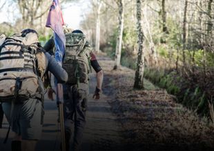 Twee wandelaars met rugzakken lopen over een bospad, een van hen draagt ​​een vlag.
