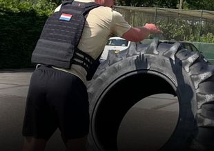 Een persoon met een verzwaard vest duwt een grote band buiten op een weg.