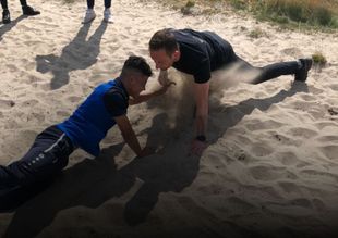 Twee mensen doen push-ups op een zandstrand, tegenover elkaar.