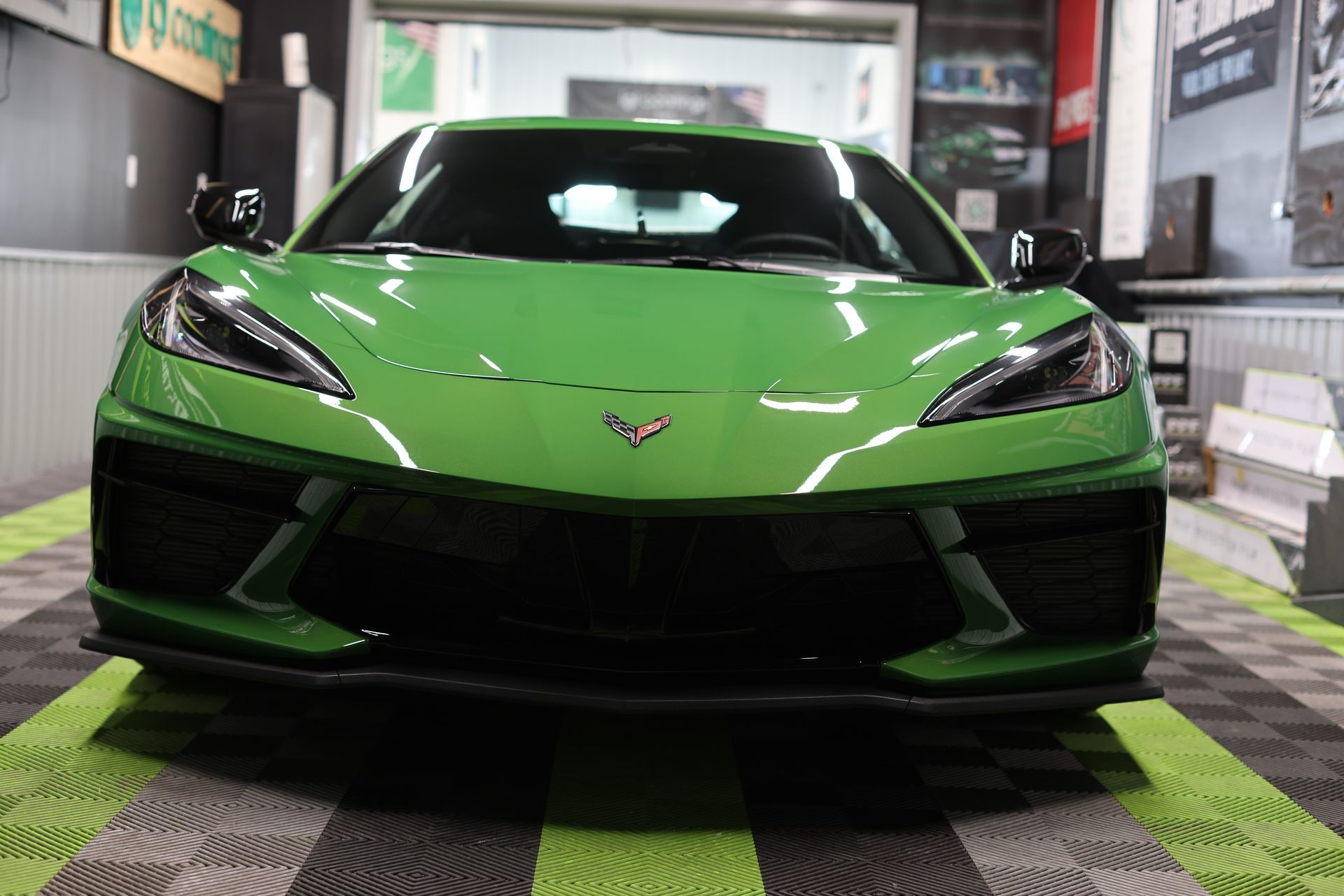 Green Chevrolet Corvette sports car in a garage, front view on a checkered floor.
