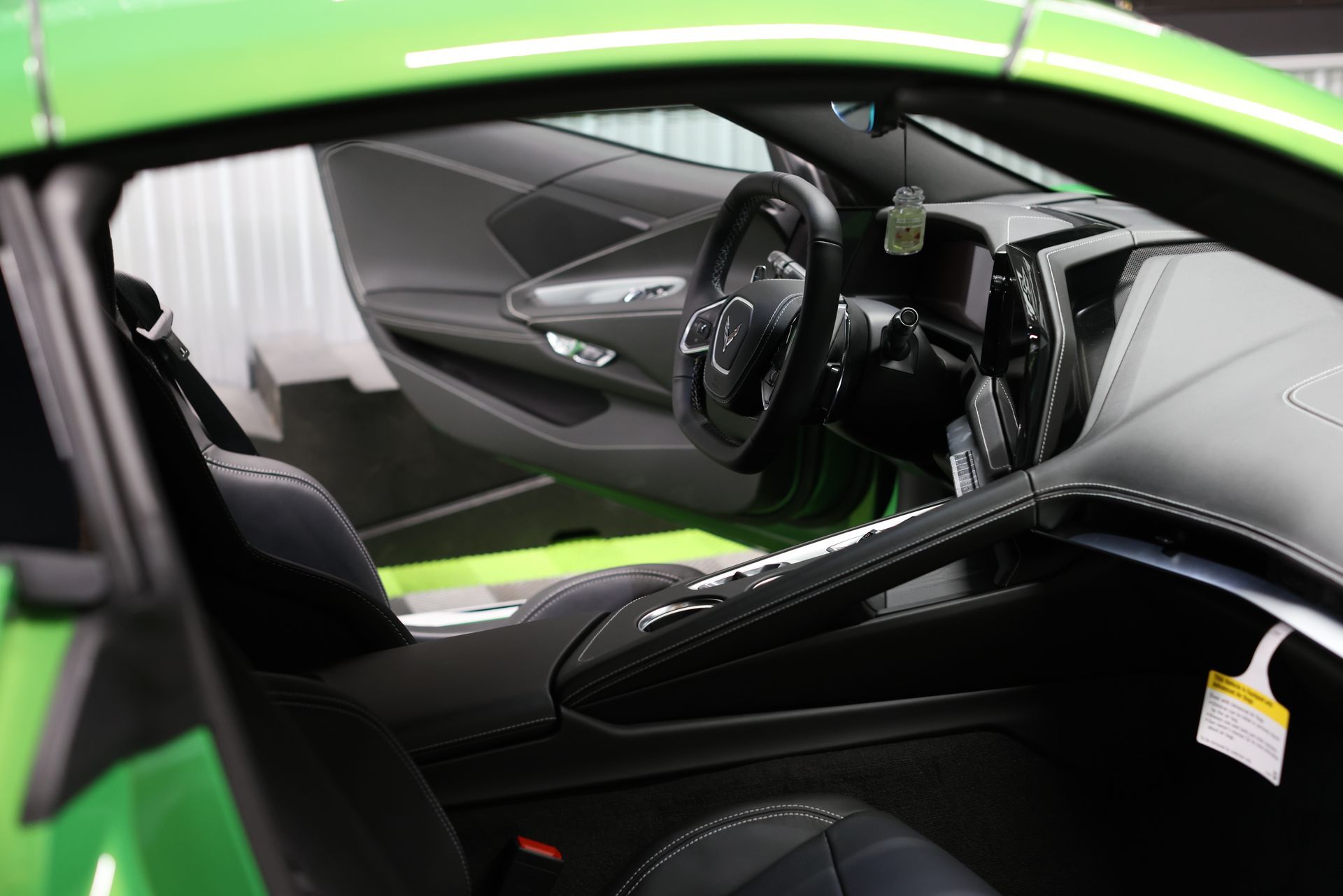 Green sports car interior with black seats and open driver door, showing steering wheel and dashboard