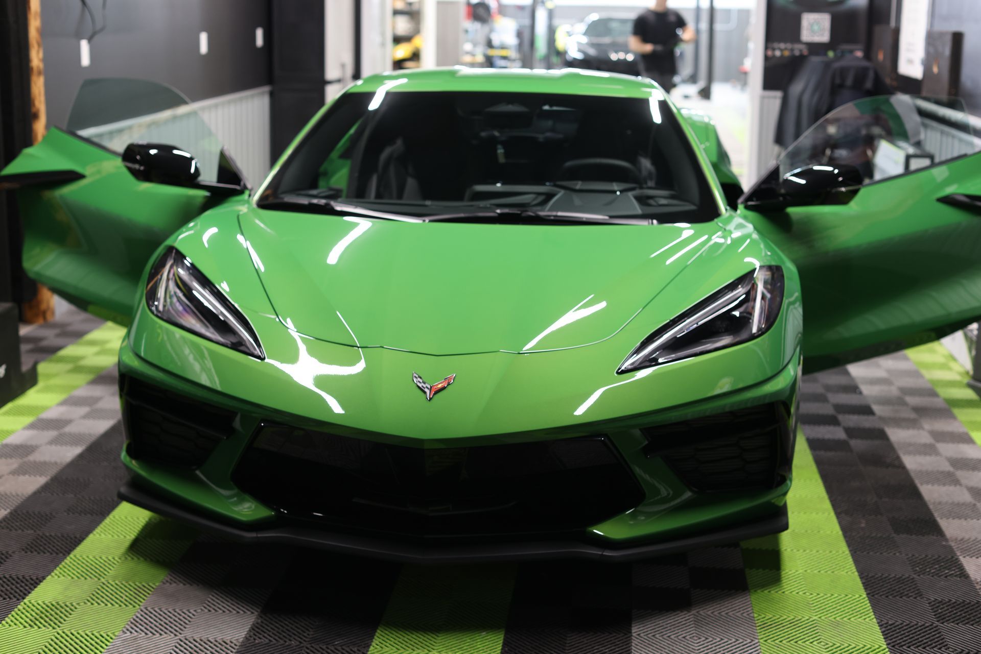 Green sports car with doors open inside a showroom, front view