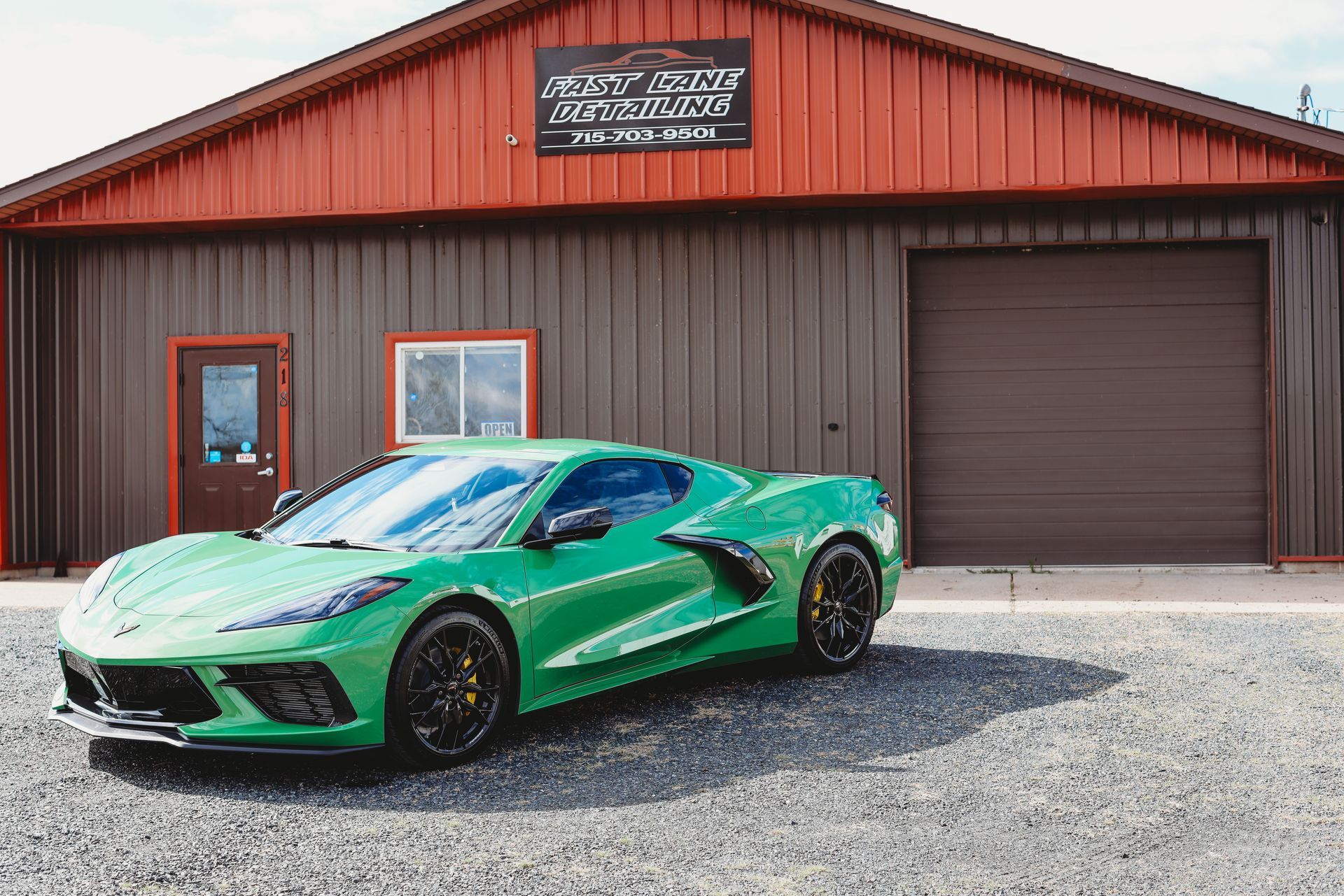 Bright green sports car parked outside a brown garage with a red roof on a gravel lot