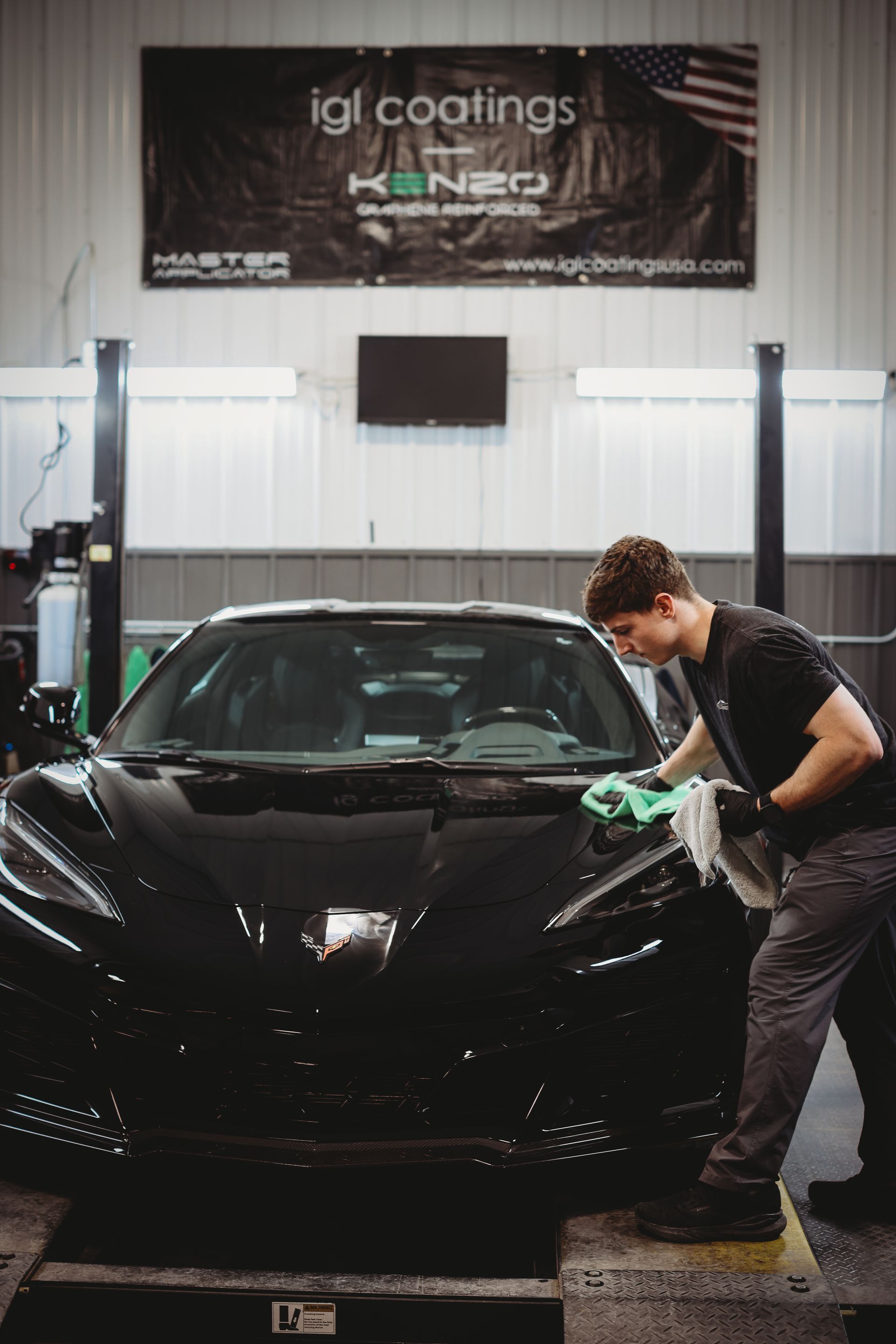 Detailing shop scene with a man polishing a black sports car under an IGI Coatings banner