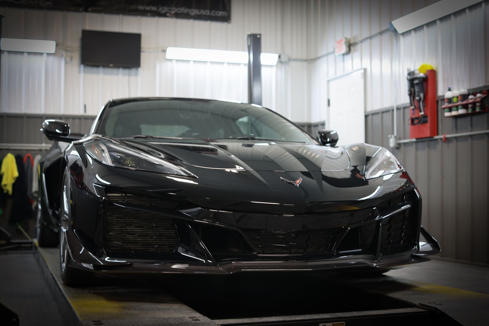 Black sports car in a garage, viewed from the front with glossy bodywork and sharp headlights.