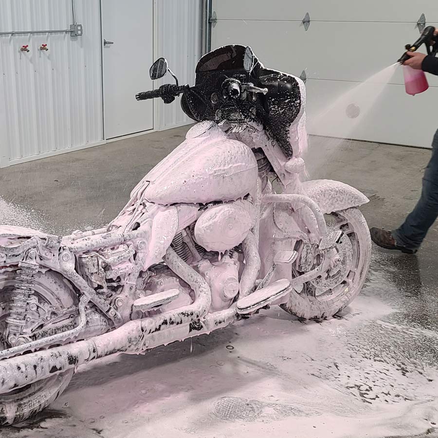A person is washing a motorcycle with foam in a garage.