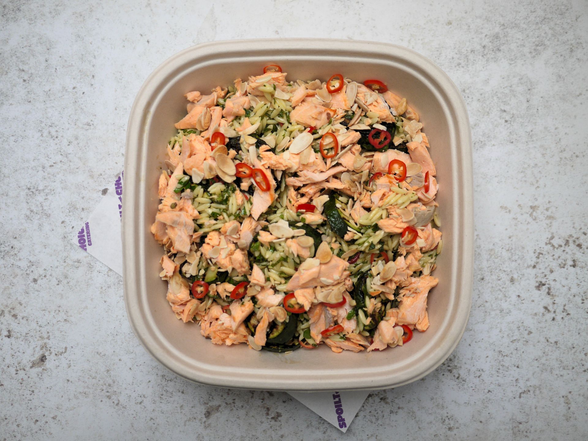 A tray of food in paper containers with wooden utensils on a wooden table.