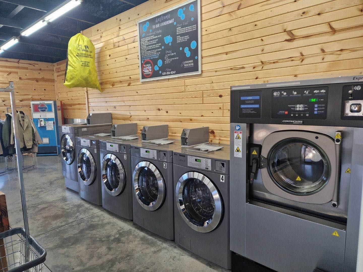 Row of industrial washing machines and dryers inside a laundromat with wood-paneled walls