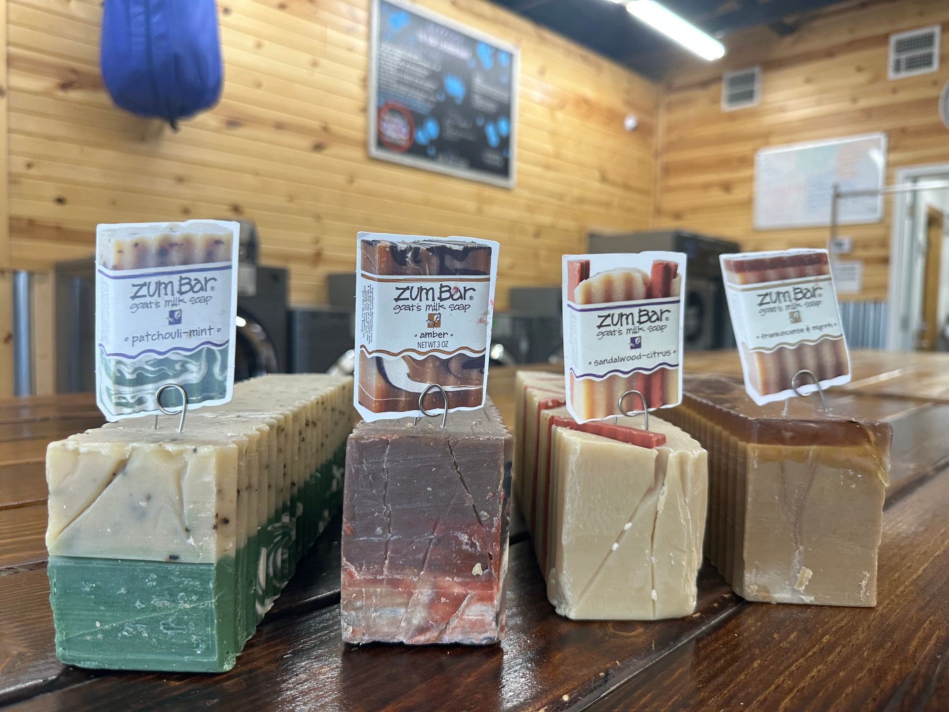 Assorted handmade soap bars with labels displayed on a wooden counter in a shop.