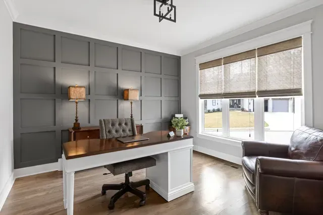 A home office with a desk , chair , lamps and windows.