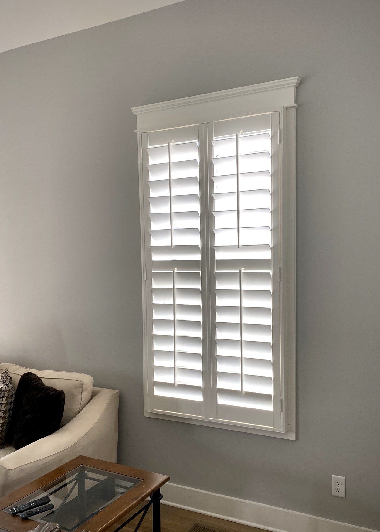 A living room with a couch and a table and a window with shutters.