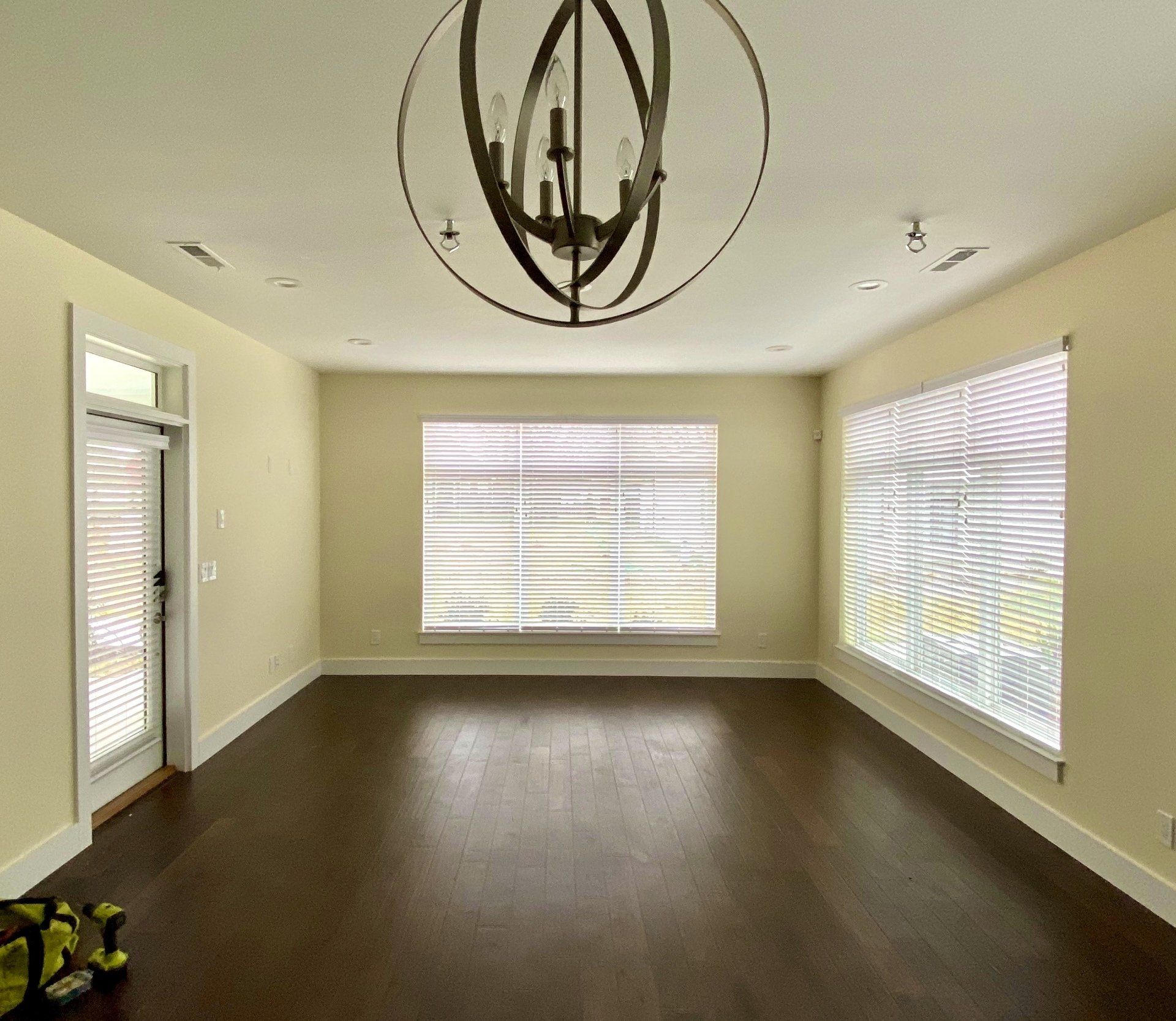 An empty living room with hardwood floors and a chandelier hanging from the ceiling.