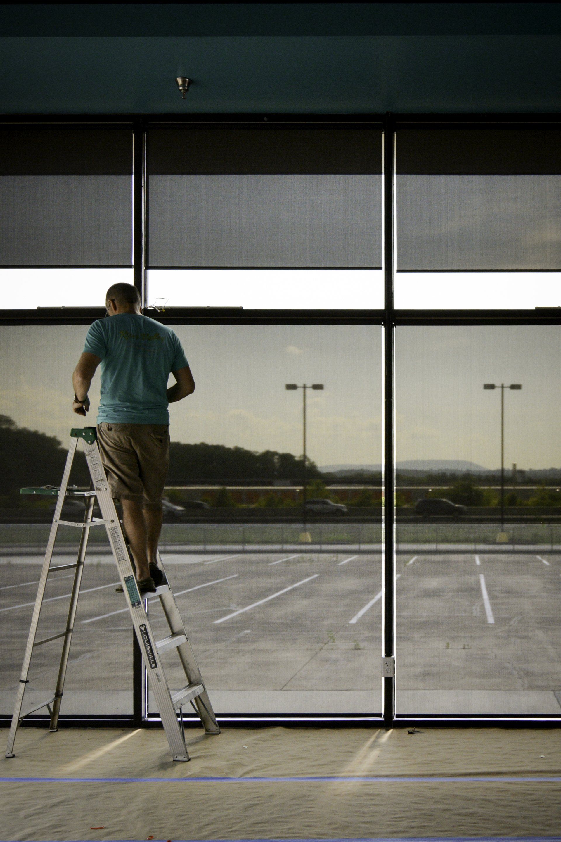 A man is standing on a ladder looking out a window.