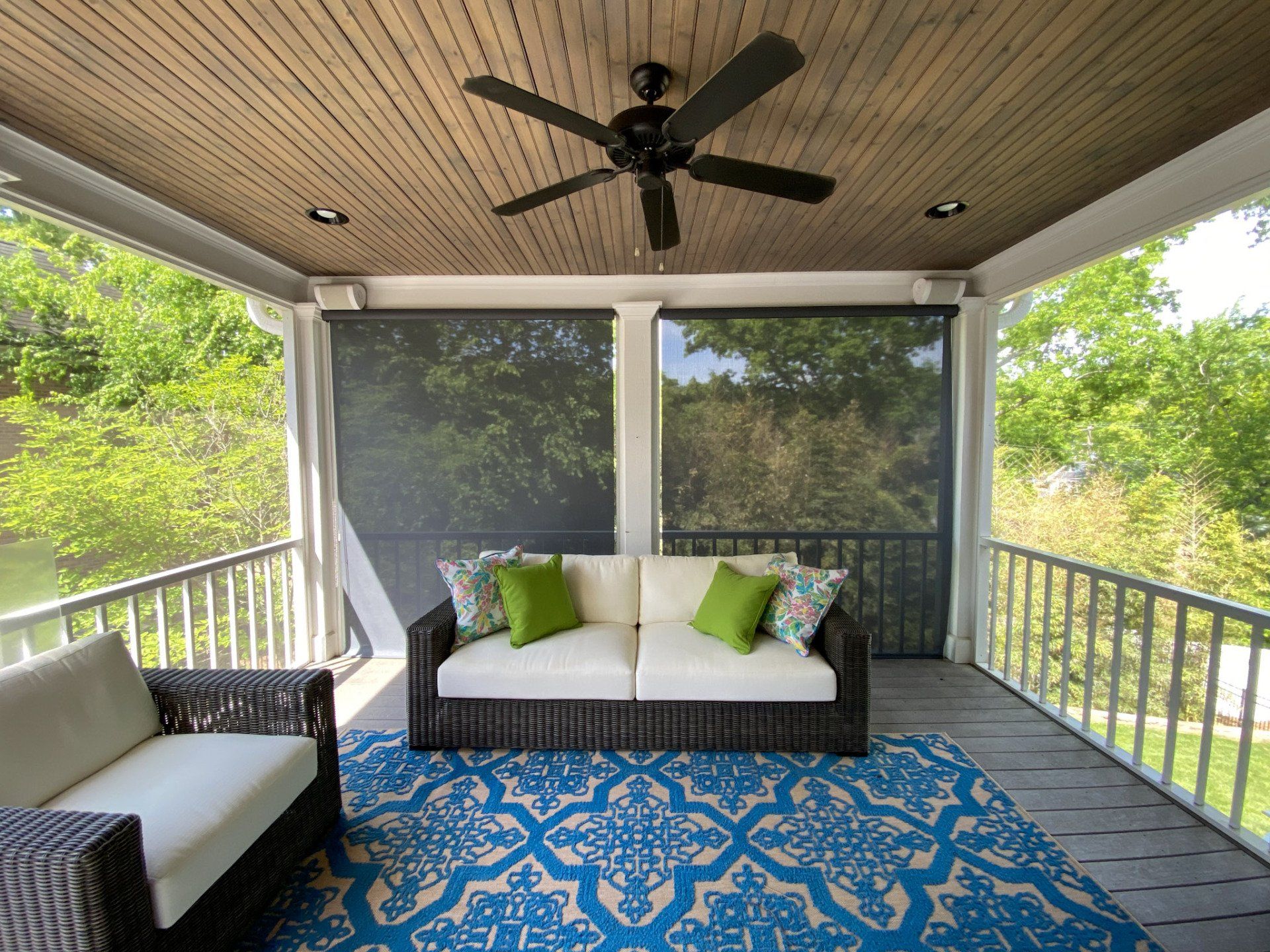 A screened in porch with a couch and chairs and a ceiling fan