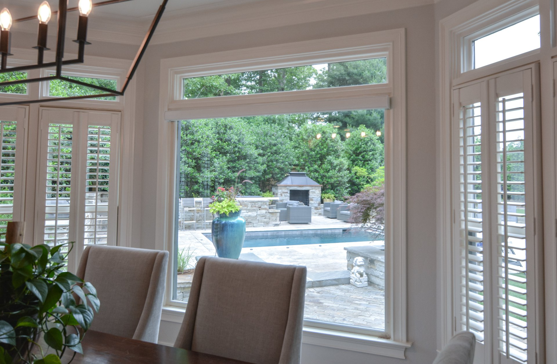 A dining room with a table and chairs and a large window overlooking a pool.