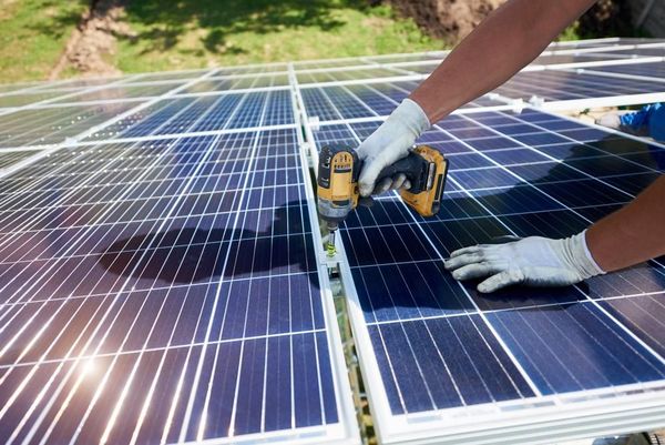 A Man is Installing Solar Panels on a Roof With a Drill — Innovo Electrical & Solar In Thebarton, SA