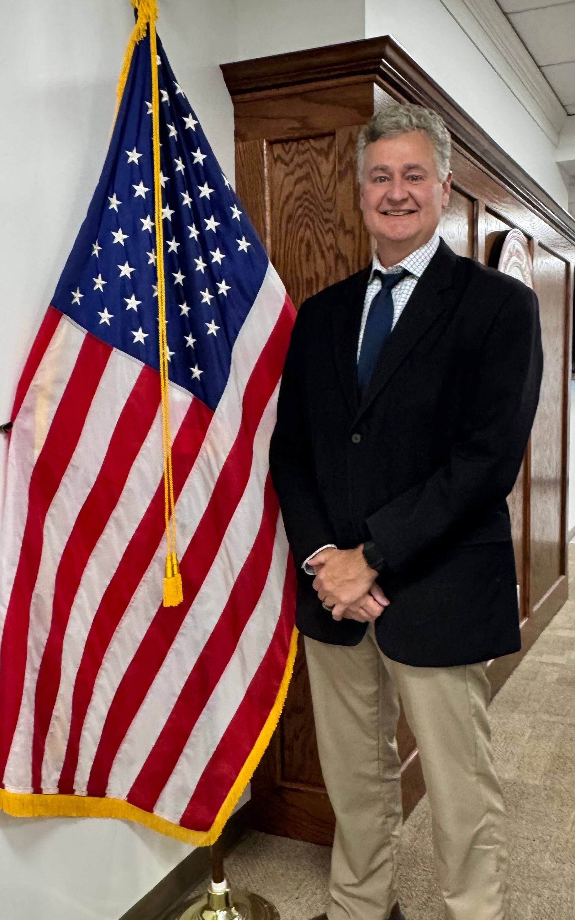 A man in a suit and tie is standing in front of an american flag.