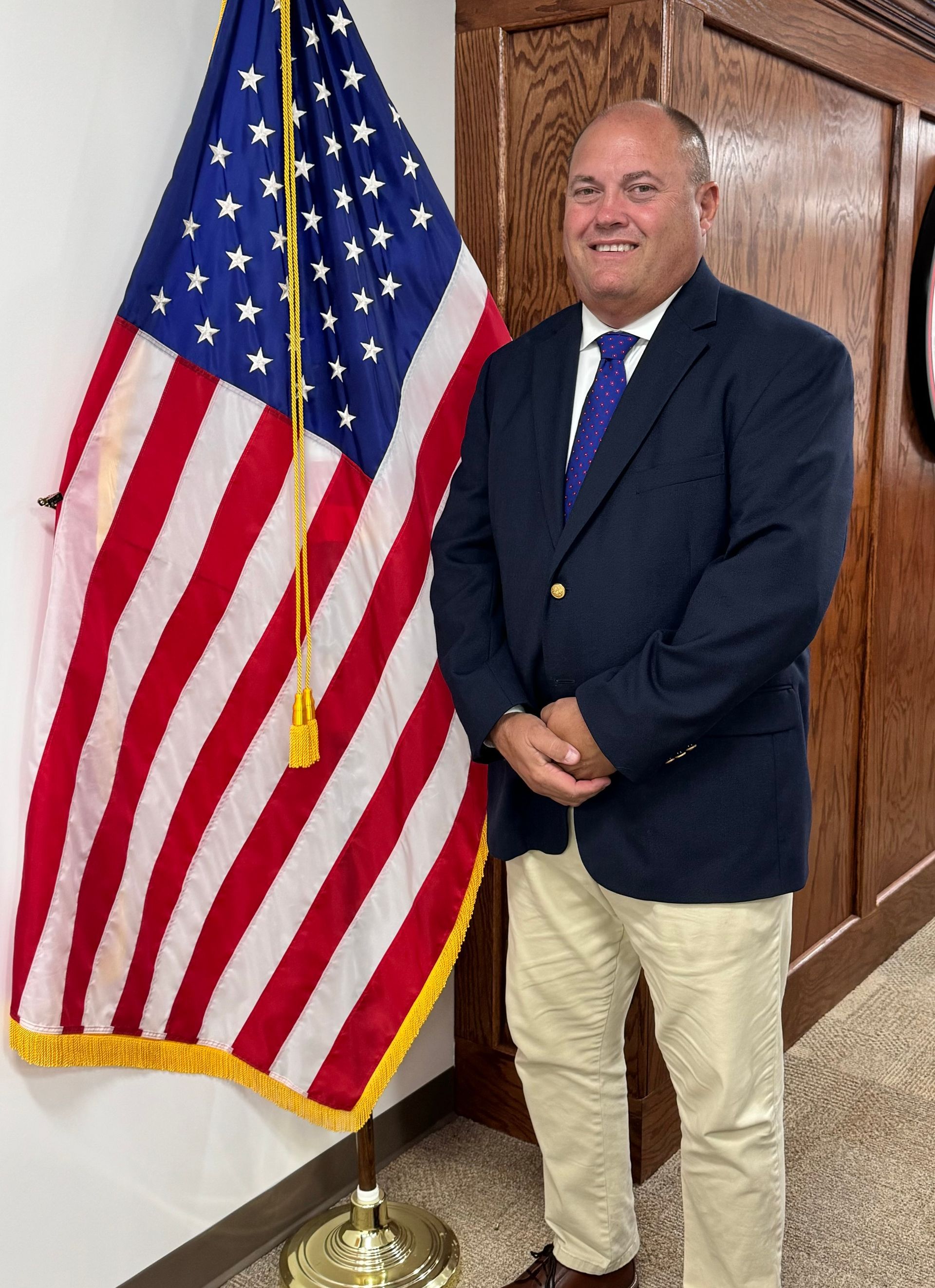 A man in a suit and tie is standing in front of an american flag.