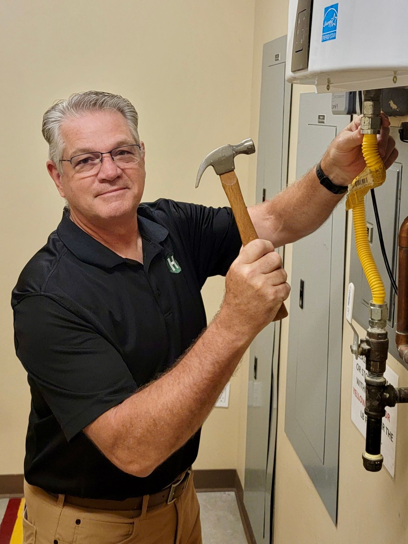 Man in black shirt using a hammer on an open electrical panel in a utility room