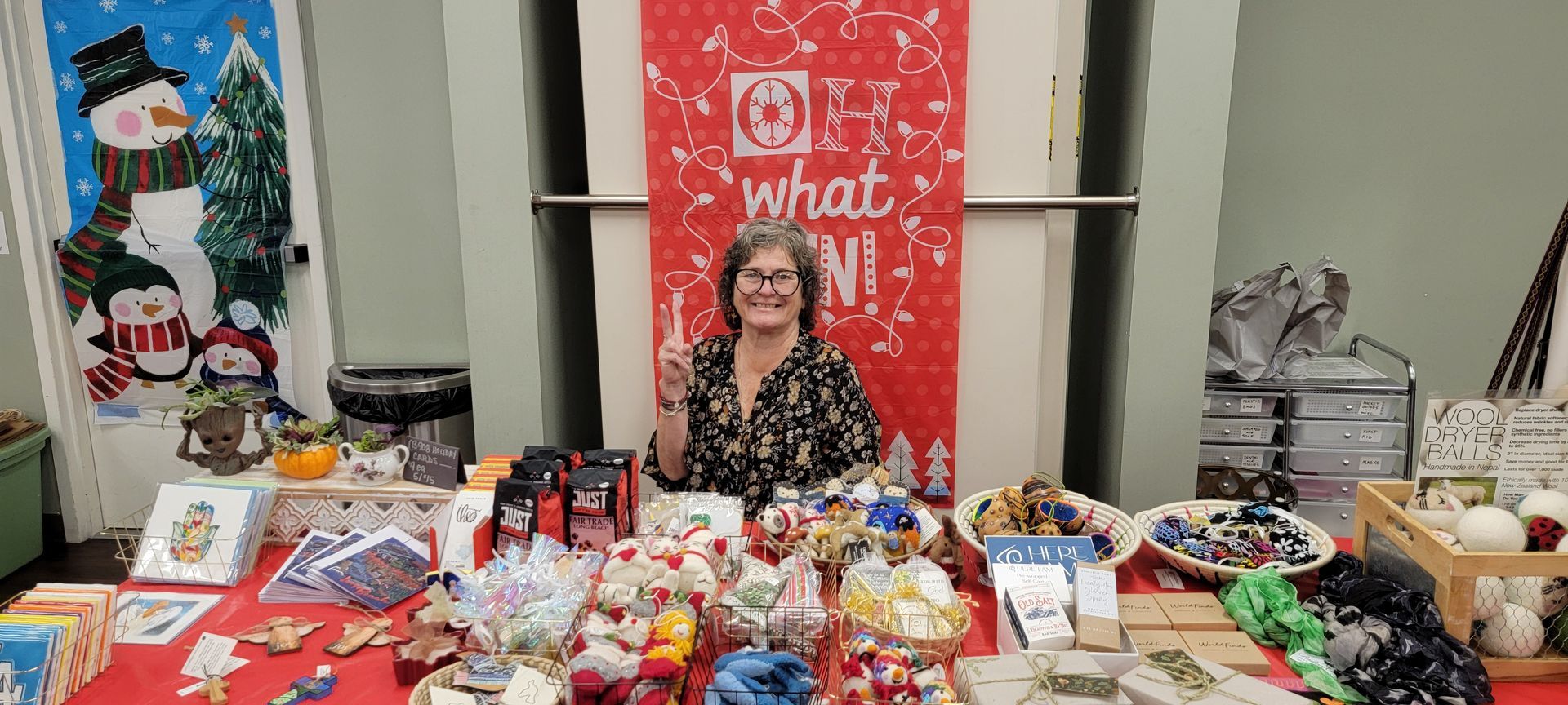 Vendor smiling behind a table of holiday treats and crafts at a festive market booth
